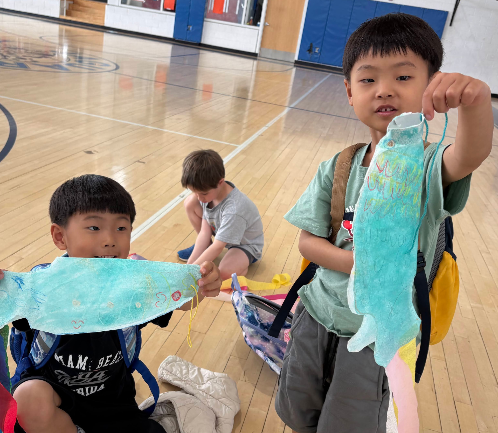 Two students in the gym holding up handmade koinobori fish streamers they painted