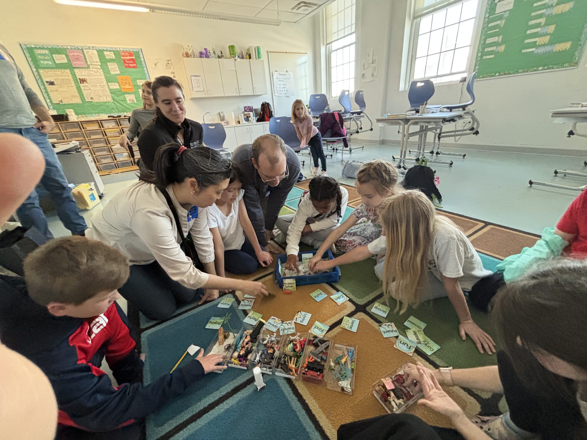 A Janney+ teacher and students gathered on the rug sorting character-word cards together