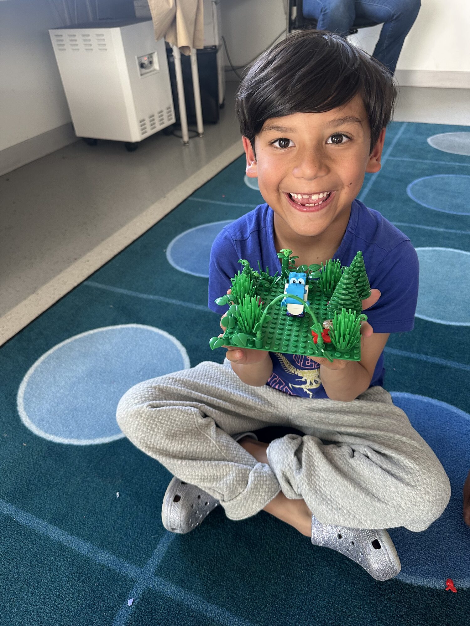 A Janney+ student proudly showing a green LEGO garden he built