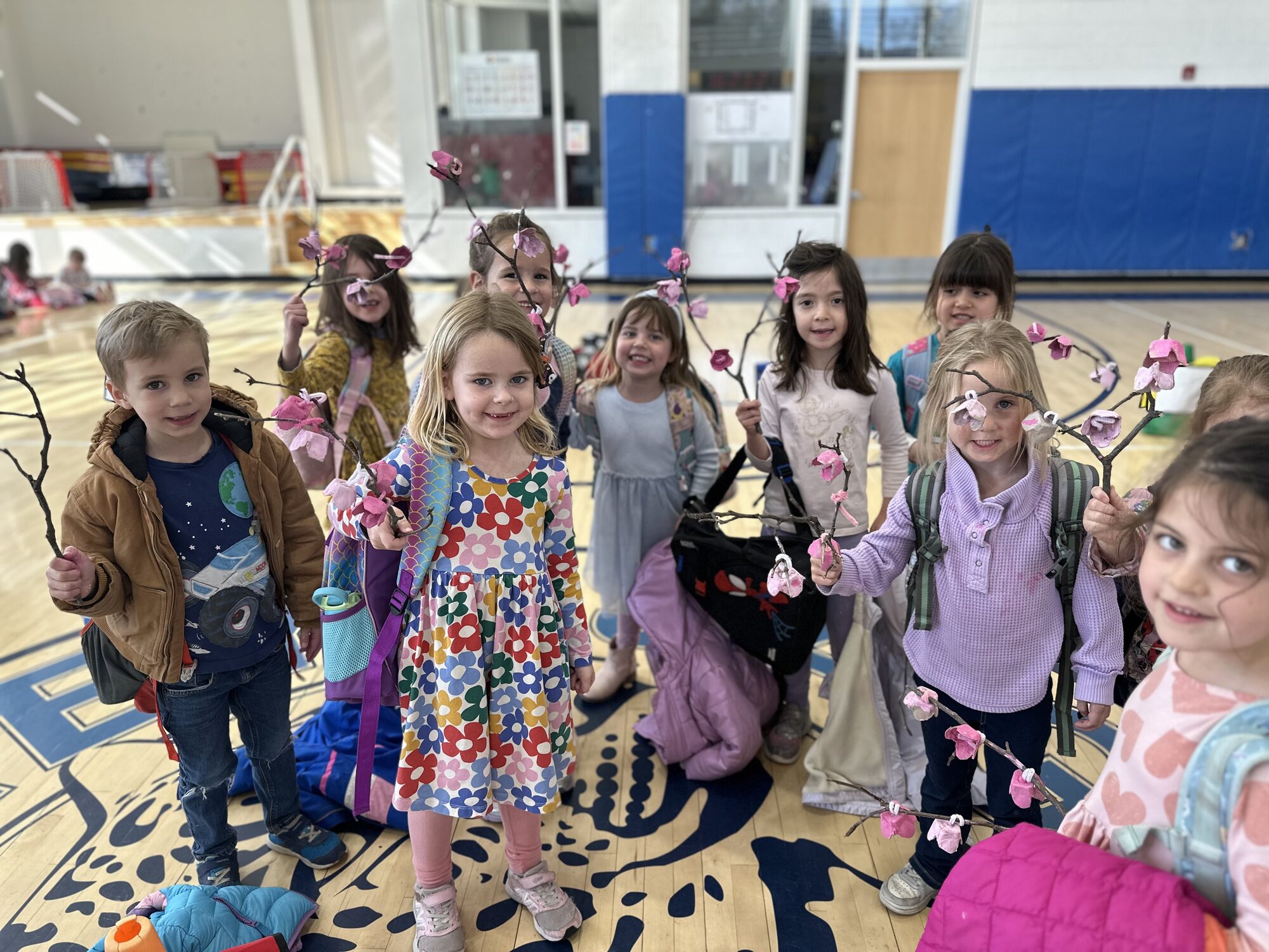 Younger Janney+ students holding up handmade cherry-blossom branches in the gym